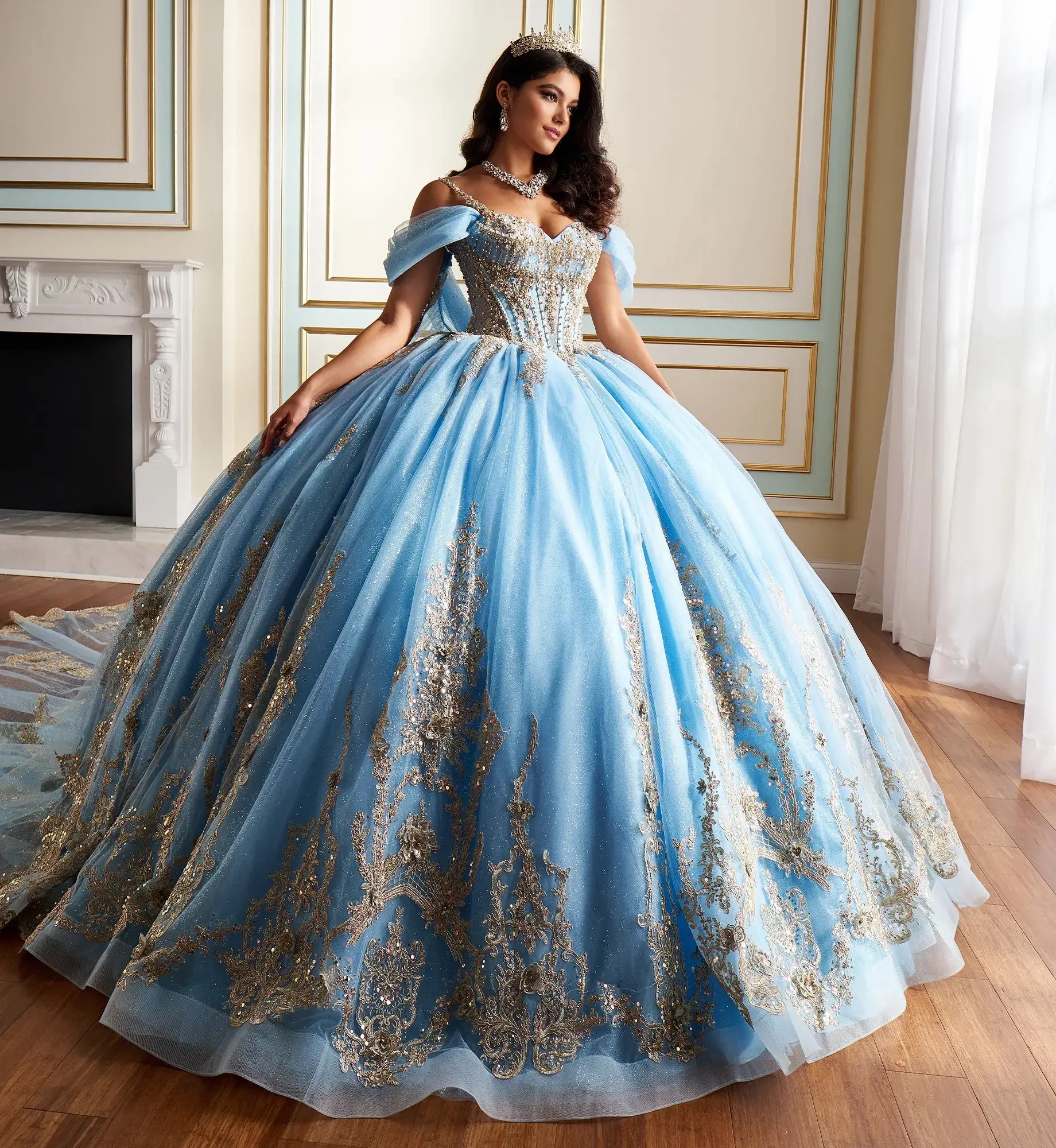 Model is wearing a light blue and gold quinceanera dress with off the shoulder sleeves