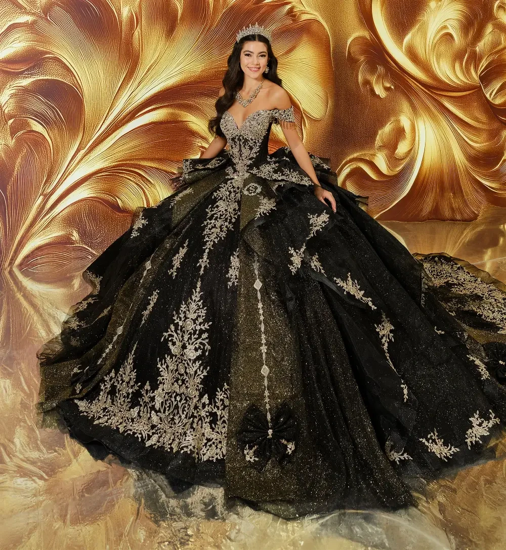 A woman wearing an elaborate black and gold gown with intricate designs, adorned with a tiara and jewelry, posed against a golden floral background.