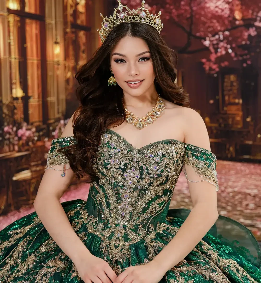 A woman in an ornate green gown adorned with intricate embellishments, wearing a crown and jewelry, smiling in a decorated setting.